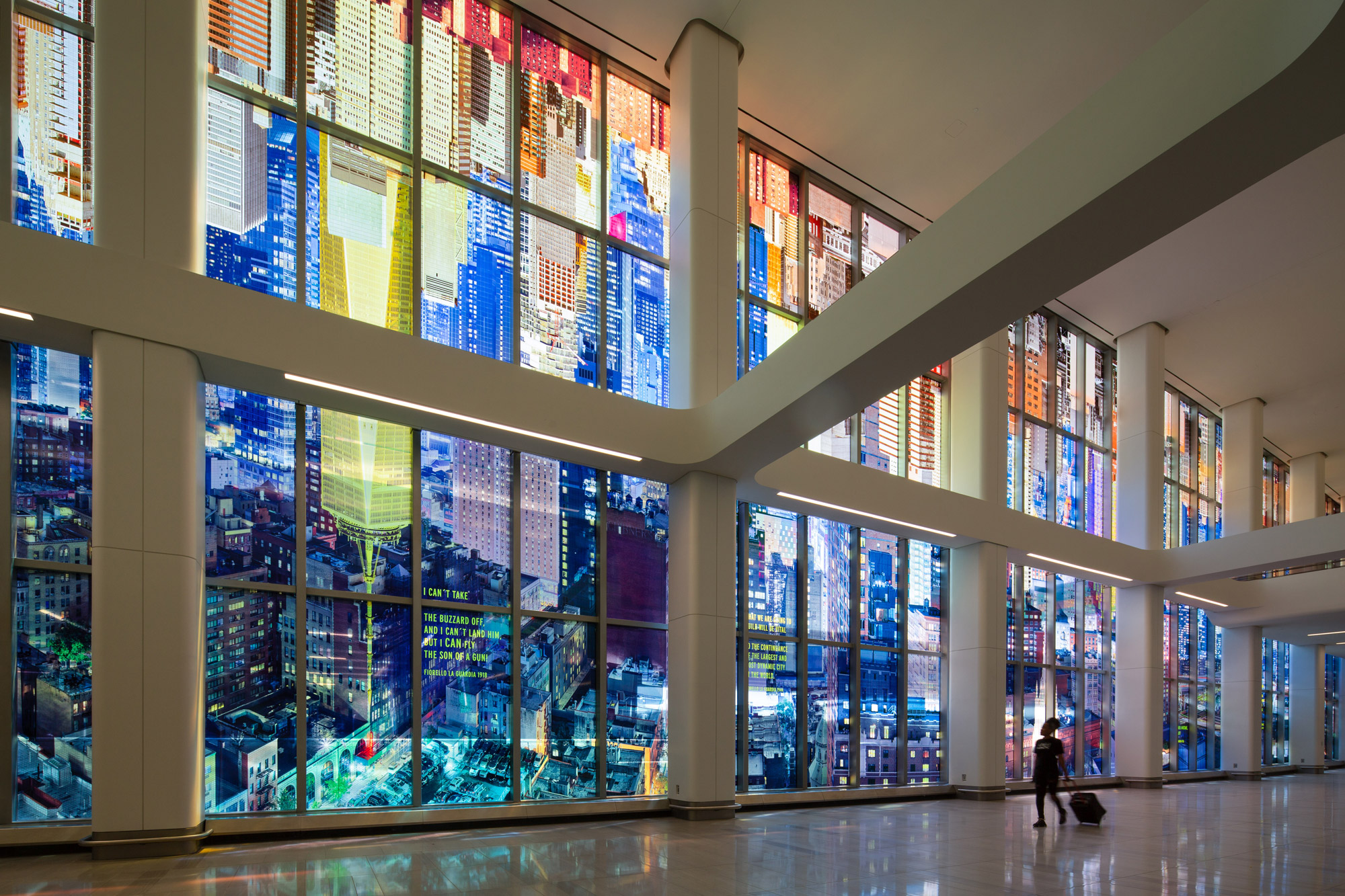 A kaleidoscopic wash of a colorful photo-collaged cityscape fills the length of two stories of tall glass windows in an airport terminal interior.