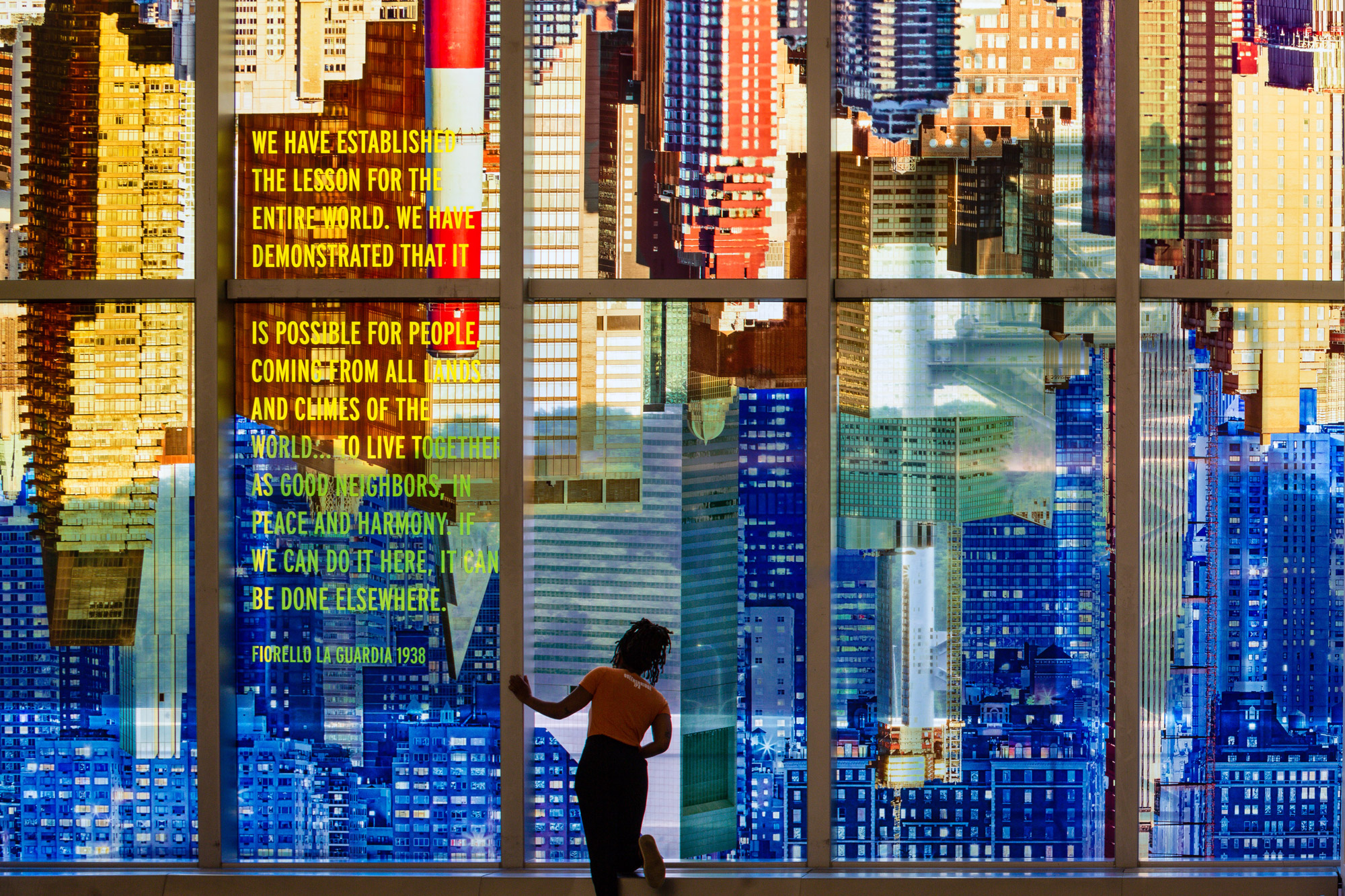 A colorful photo-collaged cityscape and text fills the length of tall glass windows in an airport terminal interior.
