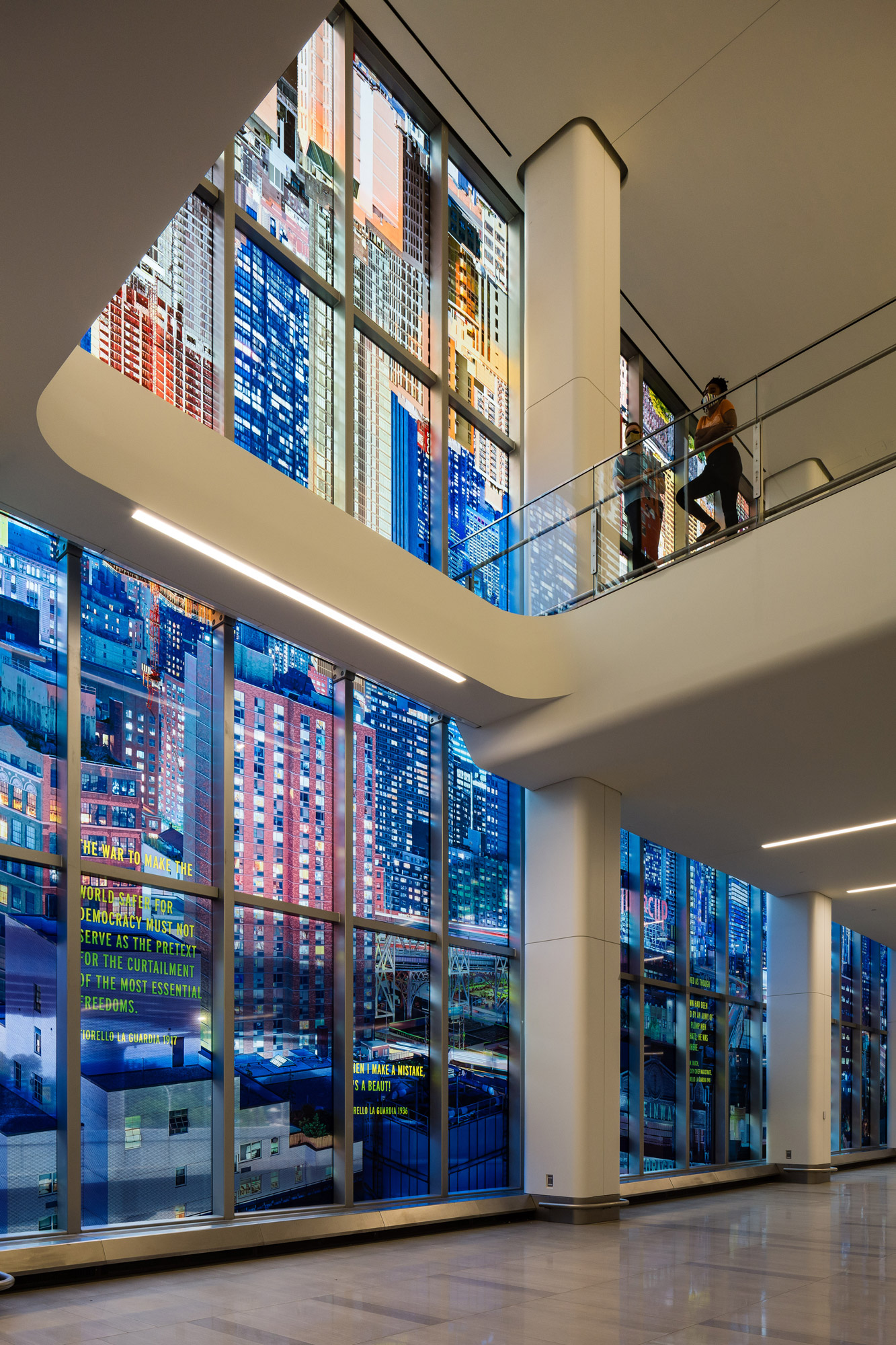 A kaleidoscopic wash of a colorful photo-collaged cityscape fills the length of two stories of tall glass windows in an airport terminal interior.