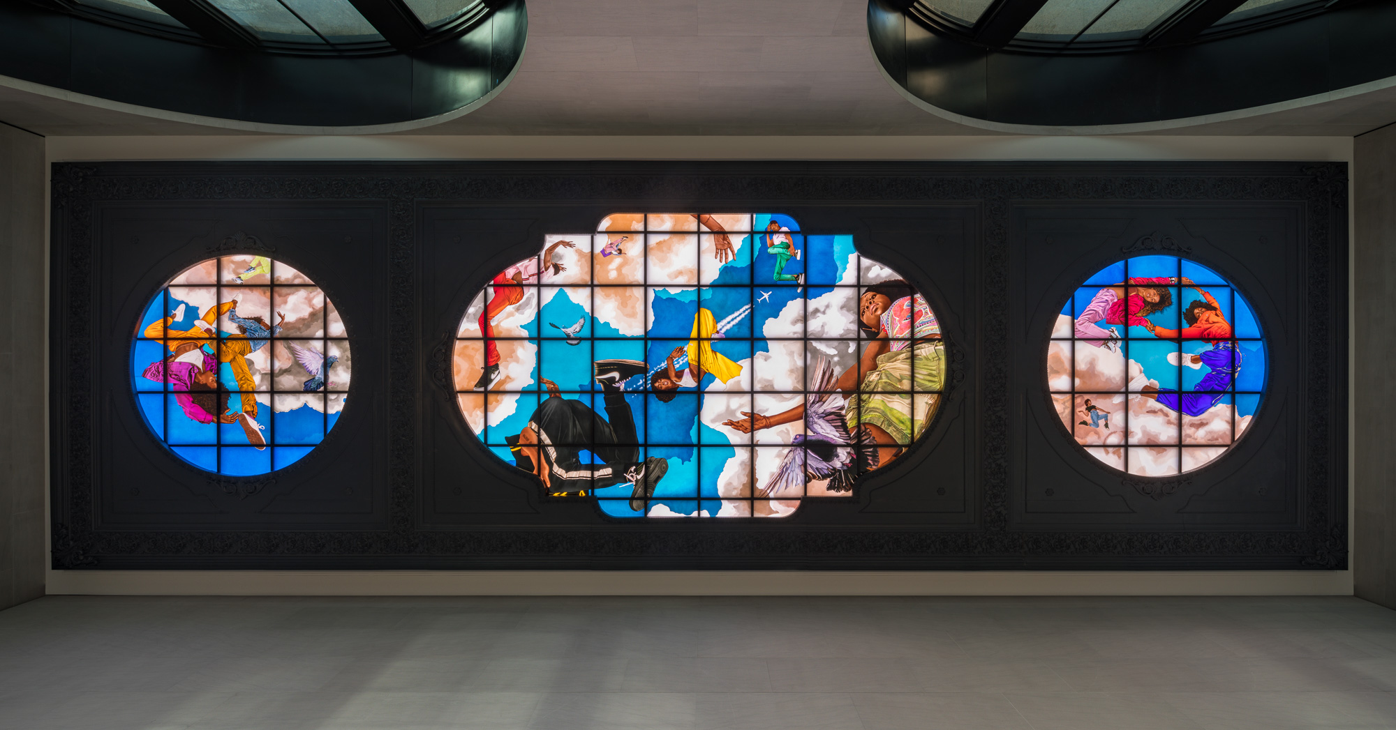 A brightly painted stained glass triptych depicting young Black people in poses drawn from breakdance, set against billowing clouds in a brilliant blue sky.