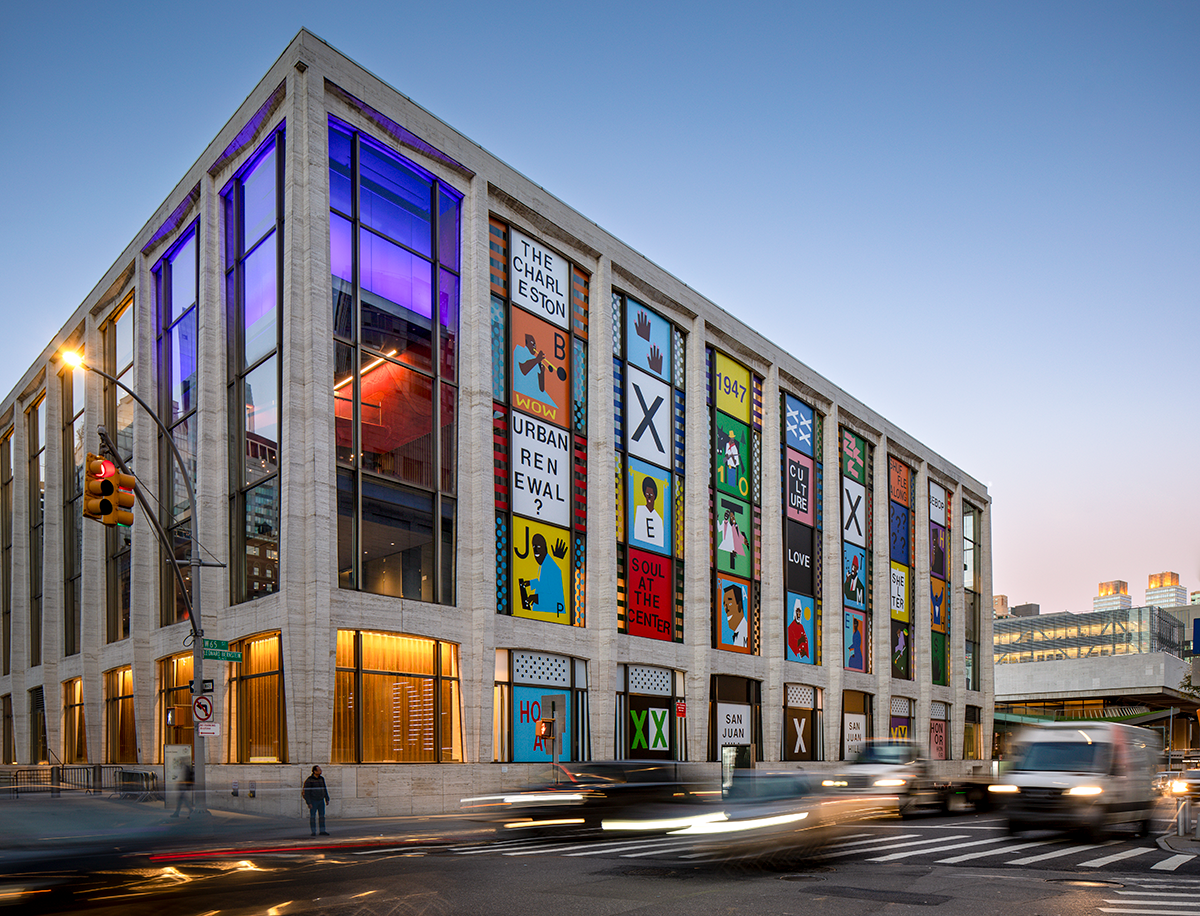 A composition of colorful, graphic portraits of significant San Juan Hill figures and historical references on the façade of a rectangular music hall in a bustling...