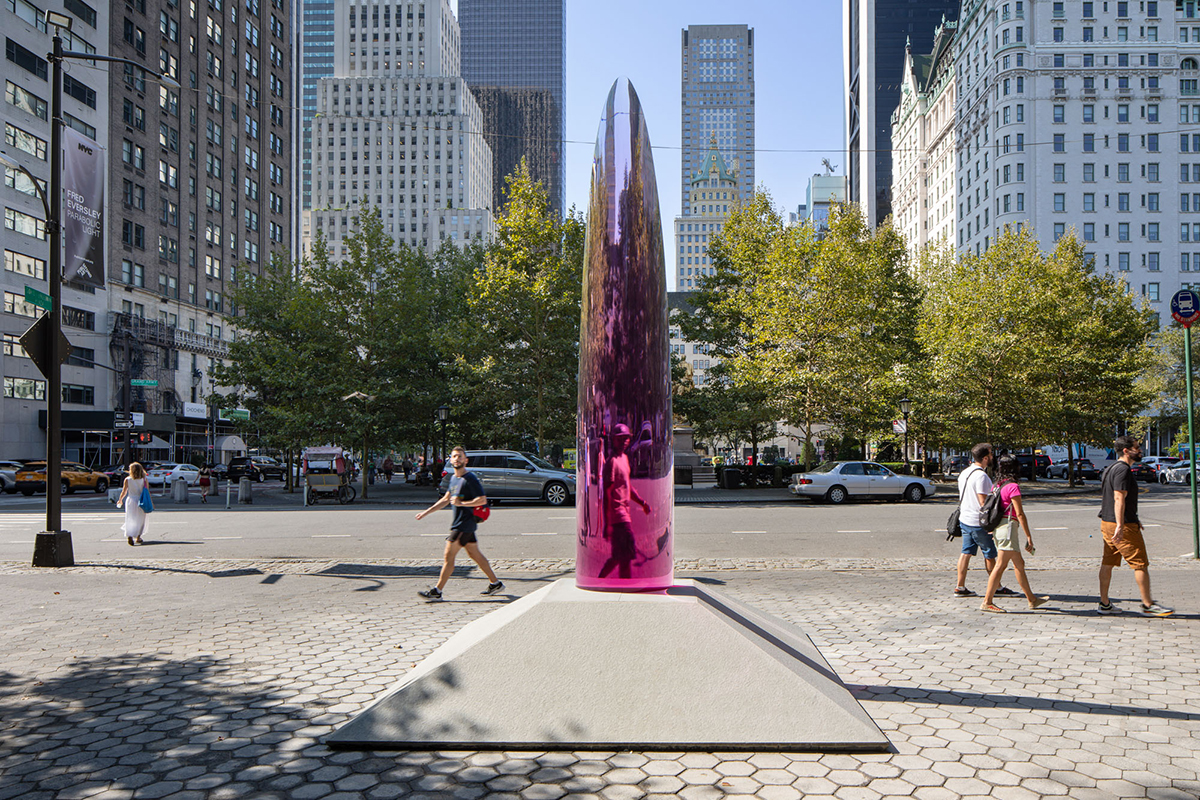 A 12-foot tall translucent and reflective magenta parabolic sculpture inhabits a park in a bustling city.