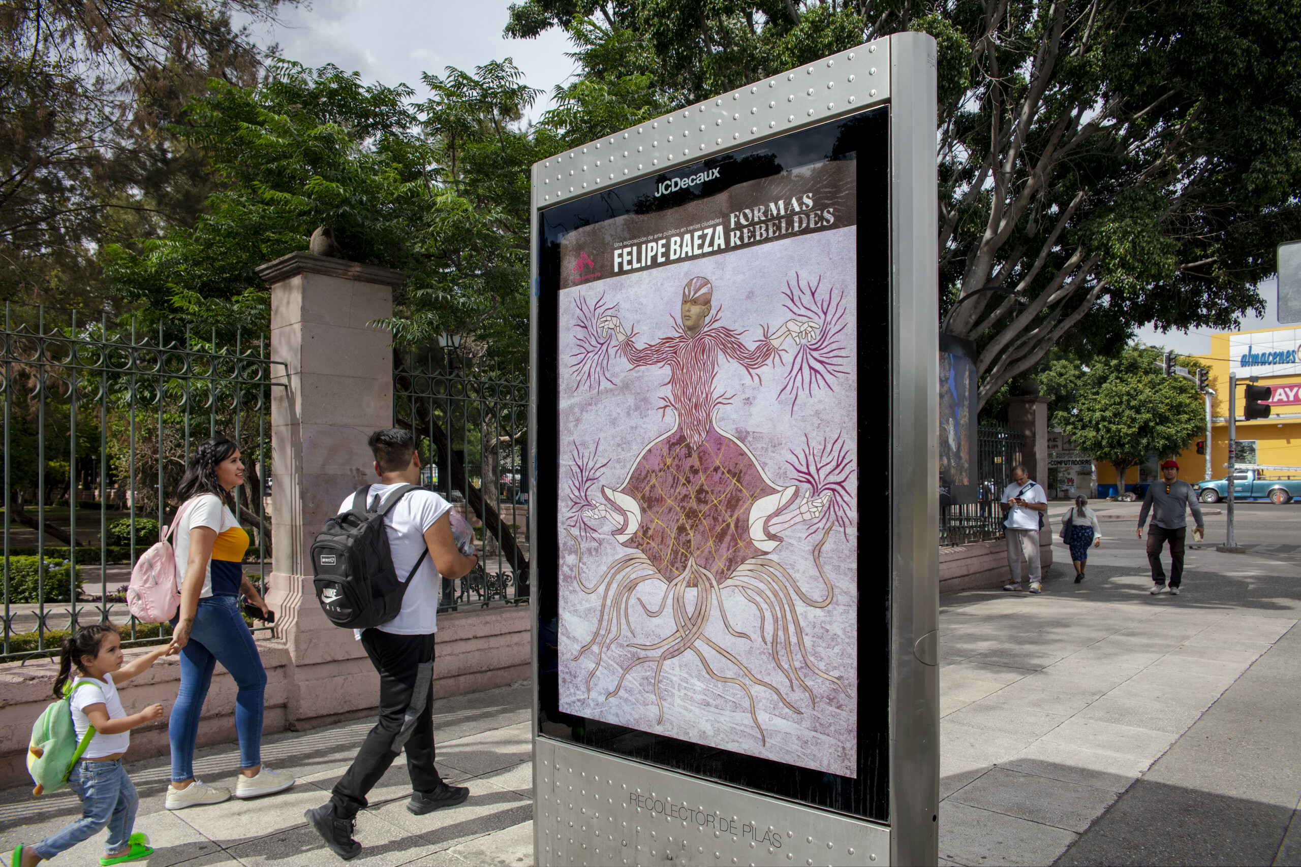Pictured on a bus shelter on a busy city street is a layered hybrid figure that merges human, artifact, animal, and vegetation. The single symmetrical figure is...