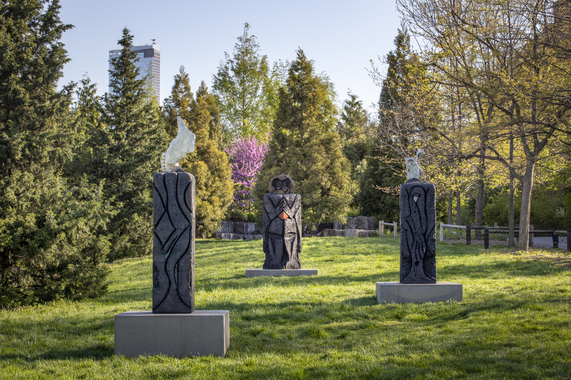 Three patinated bronze sculptures, each with a square concrete base, installed along a grassy terrace. On top of each sculpture sits a recreated skeletal structure:...